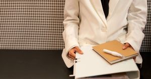 Close-up of a business professional in a white suit holding documents in a modern office setting.