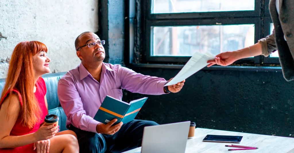 A group of professionals working together in a modern office setting, exchanging documents and ideas.