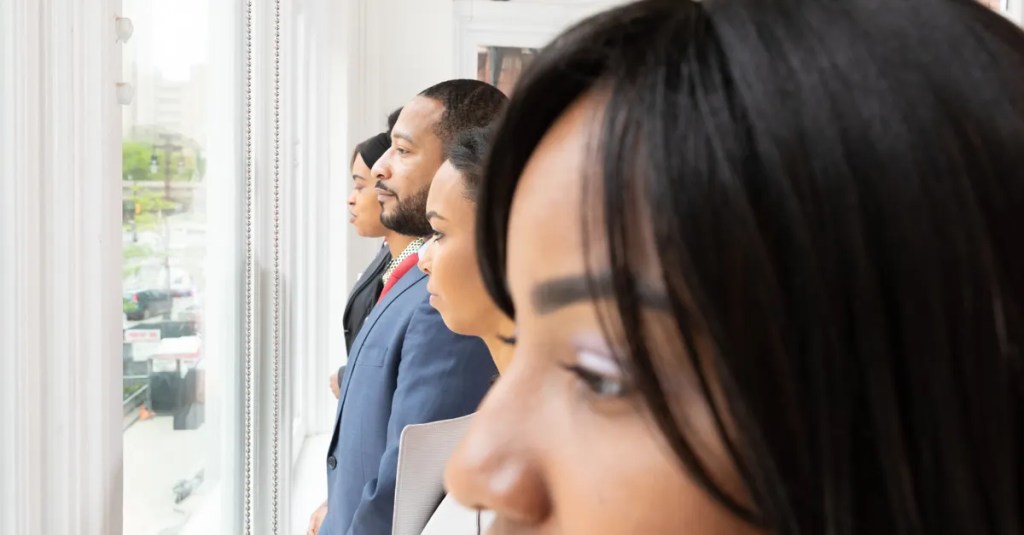 A diverse group of business professionals looking thoughtfully out of an office window.