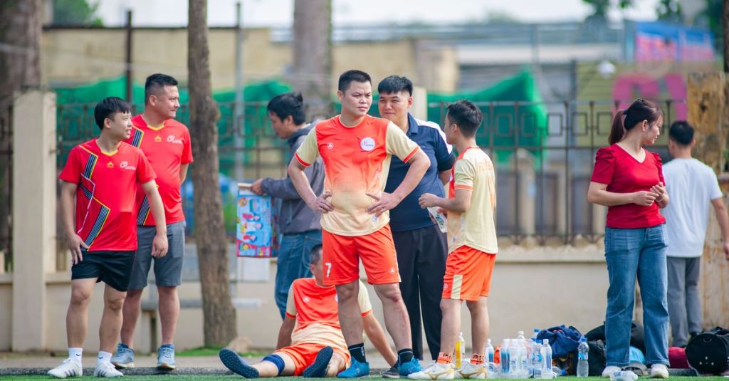 Amateur soccer team taking a break on the field in Hà Nội, engaging in lively discussion and camaraderie.