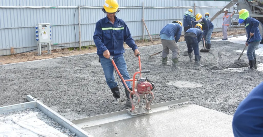 Team of workers smoothing and leveling wet concrete at a construction site.