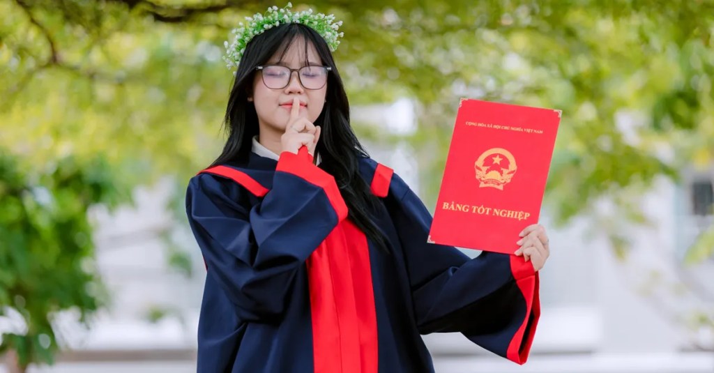 Young graduate holding diploma with a confident, joyful expression outdoors.