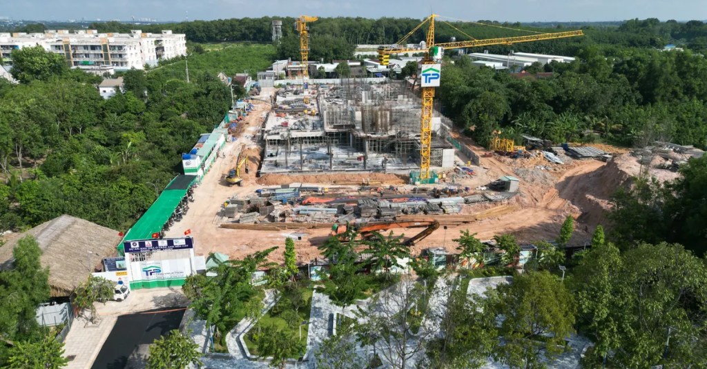 Aerial shot of an urban construction site surrounded by lush greenery under the clear blue sky.