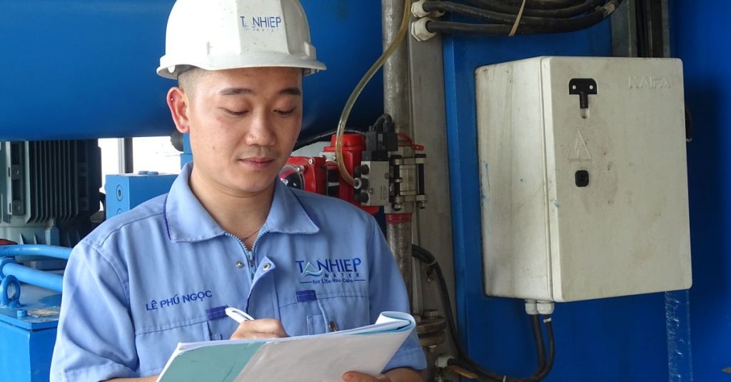 Kỹ sư mặc đồ bảo hộ kiểm tra máy móc và ghi chép trong cơ sở công nghiệp.