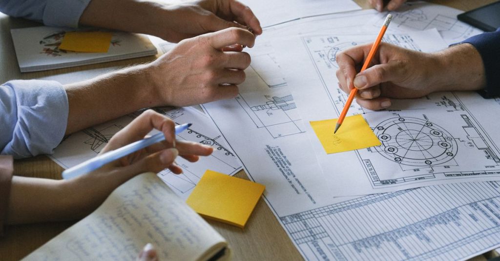 Crop anonymous coworkers sitting at table with documents and discussing project during brainstorm in light office in daytime