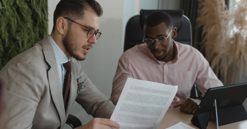 Two businessmen in an office discussing documents and working together.