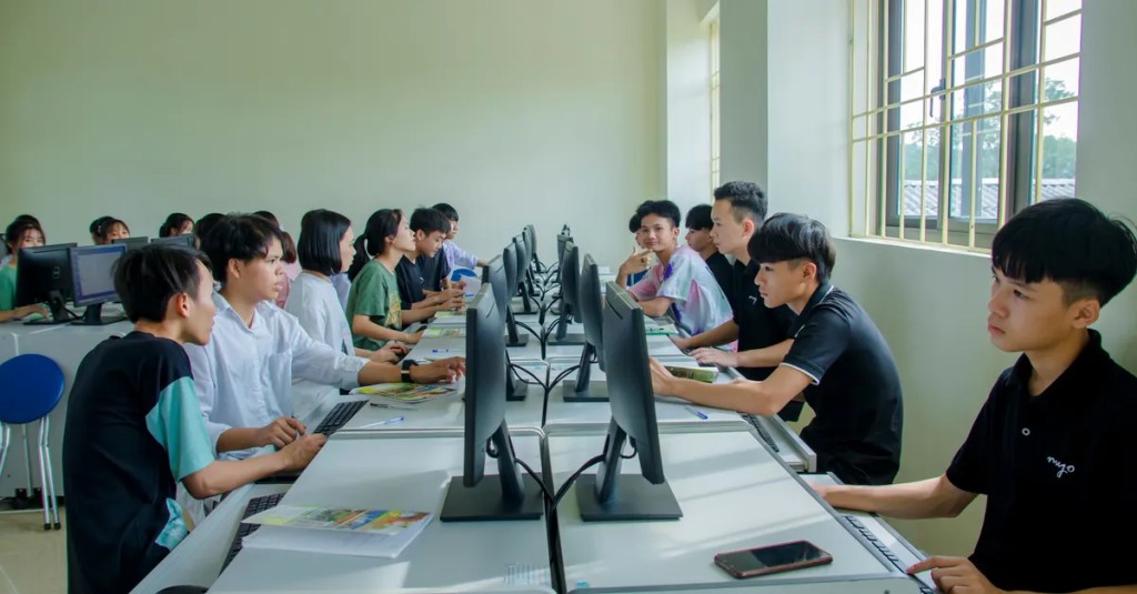 Diverse group of students studying in a computer-equipped classroom setting.