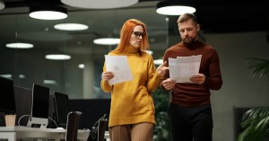 Two colleagues review documents while walking through a contemporary office space.