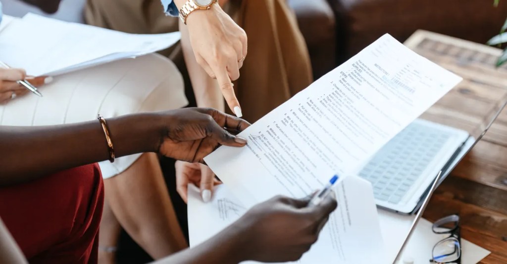 From above of crop anonymous diverse business colleagues examining data in important papers at table of office