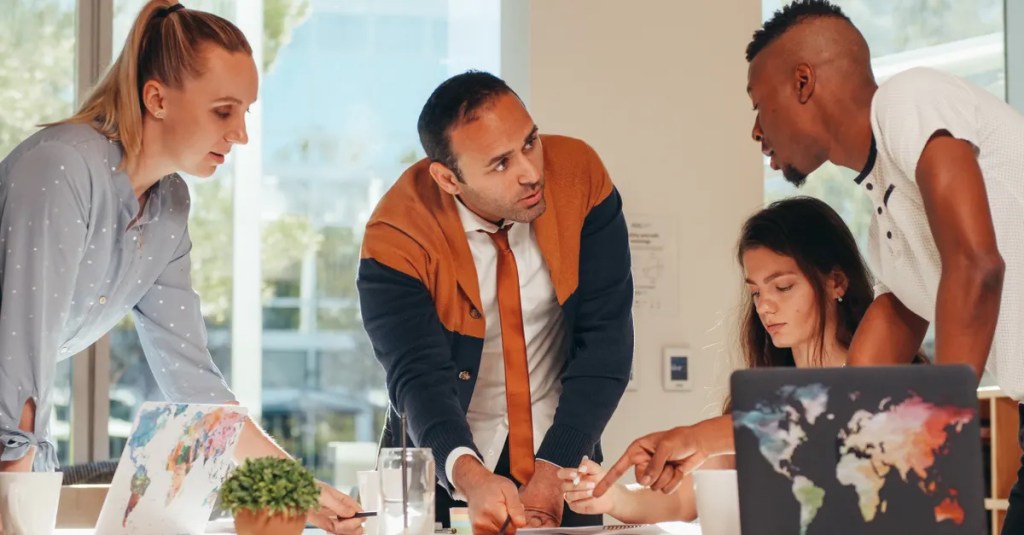 Multicultural group engaged in teamwork with laptops in a modern office.
