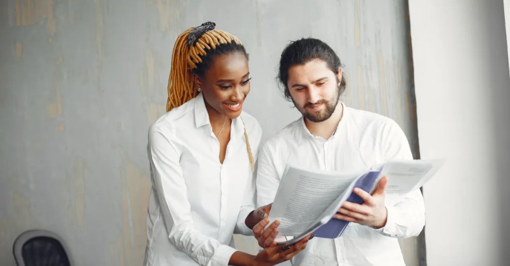 Two professionals reviewing documents in a modern office setting. Multicultural workplace.