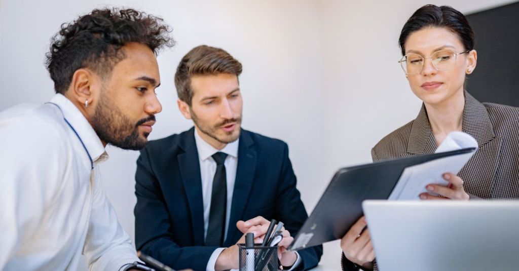 Three business professionals engaged in a focused office meeting, discussing documents.