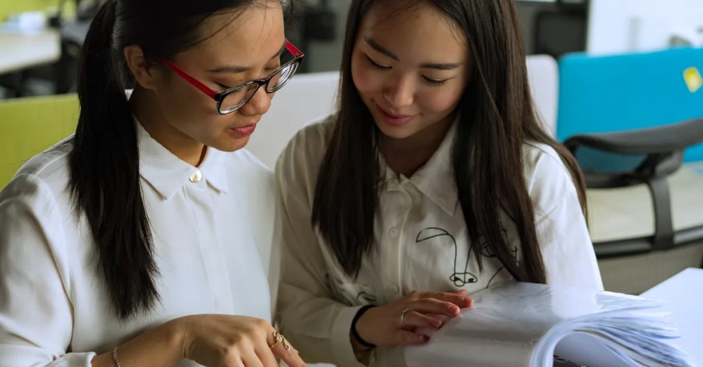 Two young women collaborating on a project in a modern office environment, emphasizing teamwork and productivity.