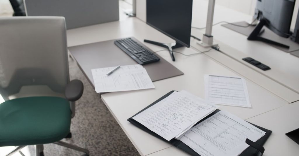 A clean and organized office desk with documents, a computer, and chair in a modern workspace.
