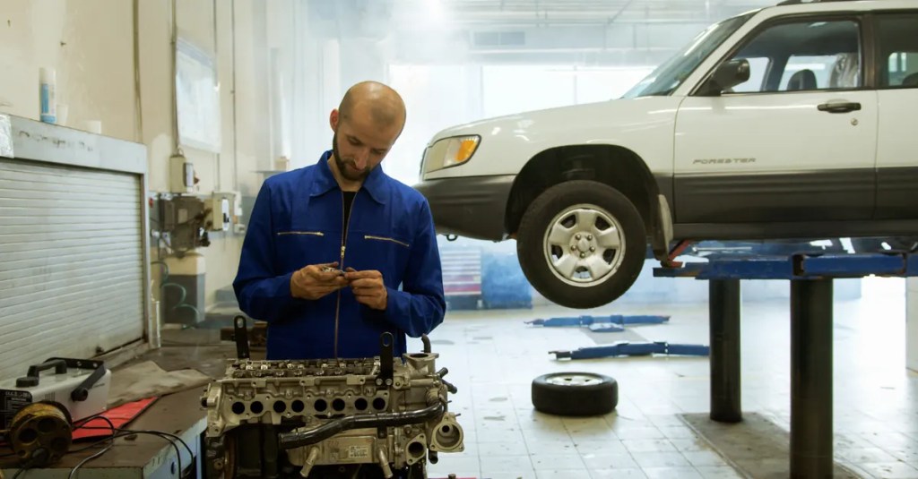 A mechanic in blue uniform inspecting an engine in a professional auto repair workshop.